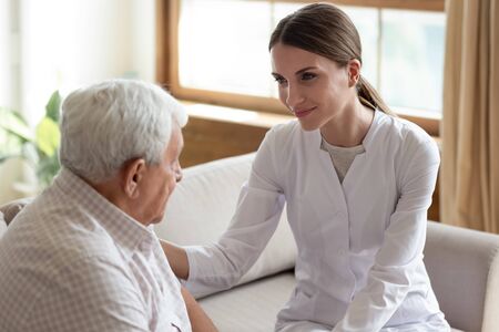 Smiling friendly woman doctor supporting older patient, caring physician wearing white uniform coat...