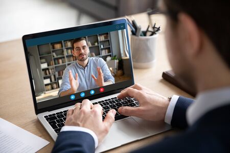 Back view of businessman talk with male business partner using video call on laptop discuss work project online, male client talk with colleague or coworker, speak on webcam conference on computerの写真素材