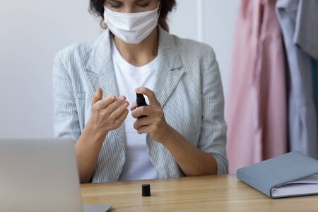 Young woman wear medical face mask use alcohol hand sanitizer protect from corona virus pandemic at workplace, female worker in protective cover pour antibacterial liquid from covid-19 coronavirusの写真素材