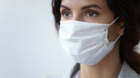 Close up of young woman wear medical protective mask from coronavirus pandemic spread, female patient in face cover look in distance hope for covid-19 virus epidemic end, healthcare, corona conceptの写真素材