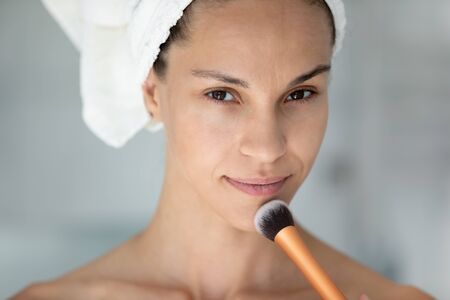 Close up portrait woman with even face tone holding make-up brush applied foundation concealer cream...
