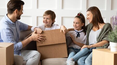 Little preschool child boy sitting in carton box, playing with happy parents and sister in living room after moving into new flat apartment. Smiling young couple having fun with children at home.の写真素材