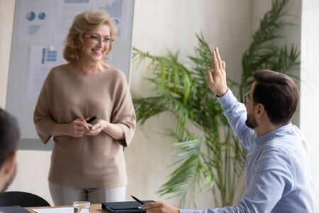 Confident male employee raise hand ask answer question at presentation or training in office, active man worker volunteer interact with female coach or presenter at briefing, cooperation conceptの写真素材