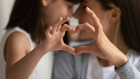 Close up of young mother and cute little daughter make heart sign with hands enjoy close tender moment together, caring mom and grateful small girl child show love and support in family relationshipsの写真素材