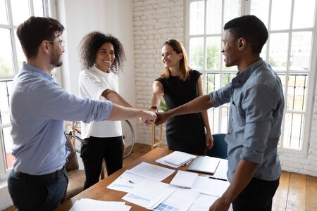 Multi-ethnic young happy associates putting fists together forming a circle, gesture of alliance,...