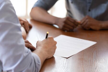 European couple during meeting with african ethnicity realtor signing rental agreement close up image, client buying first property hold pen put signature on legal paper document, make deal conceptの写真素材