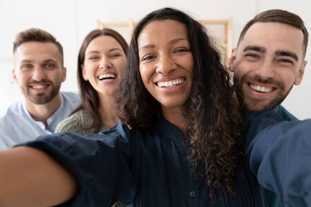 Smiling multiracial colleagues take self-portrait picture have fun entertaining together in office,...