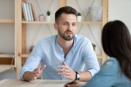 Confident young Caucasian male job candidate sit at desk talk make good first impression at interview, motivated millennial man applicant explain idea speak with business partner or client at meetingの写真素材