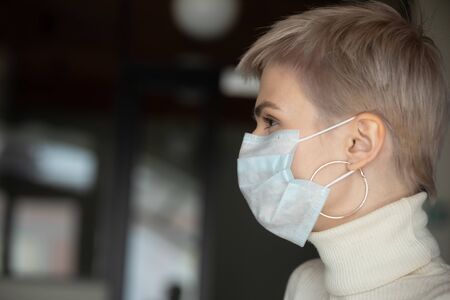 Side view close up head shot young woman with short haircut wearing breath protecting facial mask....