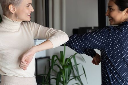 Focus on happy young female mixed race friendly colleagues bumping elbows, avoid handshaking hugs...