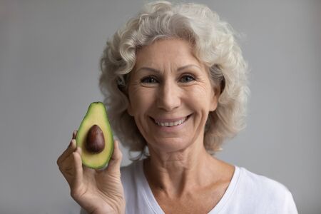 Close up head shot happy hoary senior mature retired woman looking at camera, showing avocado....