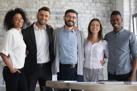 Portrait of standing in row smiling multiracial team embracing looking at camera. Happy diverse corporate staff, hugging specialists, bank workers photo shoot, HR agency recruitments.の写真素材
