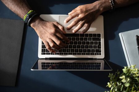 Close up top view of African American male worker busy typing on laptop keyboard at office...