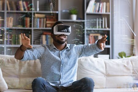 Excited African American young man in virtual reality glasses touch objects interact with 3D simulation, happy biracial male in VR goggles have fun testing new device, digital technology conceptの写真素材