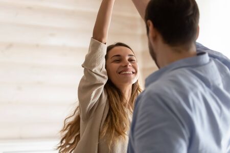Head shot young man twisting smiling joyful wife, enjoying active holiday time at home. Laughing woman dancing with affectionate husband, having fun together in living room, family couple pastime.の写真素材