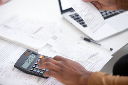Close up african american man hand using calculator and laptop for calculating finance. Businessman taxing, accounting, statistics and credit analytic for mortgage payment.の写真素材