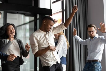 Excited happy multiracial businesspeople have fun engaged in activity in office together, overjoyed diverse colleagues dance celebrate successful business project, Friday celebration conceptの写真素材