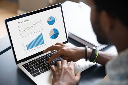 Close up of african American male worker busy working on modern laptop analyzing financial...