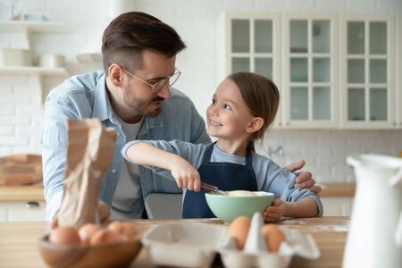 Loving young Caucasian father and cute little preschooler daughter making pancakes for breakfast at home together, happy dad and small girl child baking cooking biscuits in kitchen on weekendの写真素材