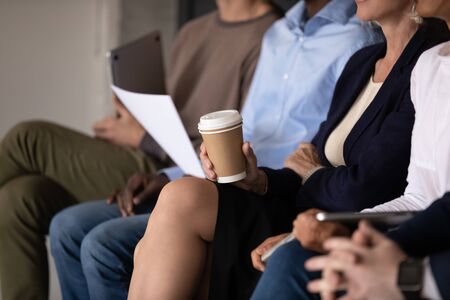 Close up of diverse job candidates sit in row waiting for work interview in office, multicultural businesspeople or applicants in queue before hiring, employment, recruitment conceptの写真素材