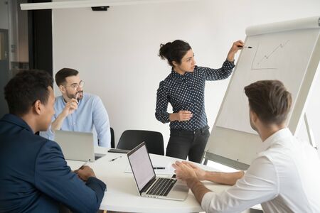 Multi-ethnic businesspeople gathered together in boardroom, staff listens lecture look at graph...