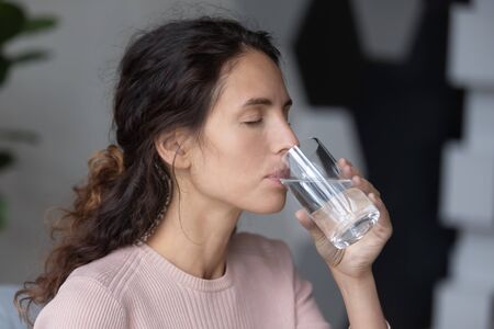 Side head shot close up view peaceful calm attractive millennial woman drinking glass of pure...