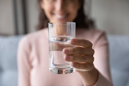 Close up happy woman pulling out hand with glass of fresh cool water. Smiling lady recommending...