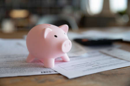 Close up pink piggy bank on wooden desk with paper domestic bills, taxes and calculator, financial accounting, money savings, loan and payment, household, manage budget plan and paperworkの写真素材