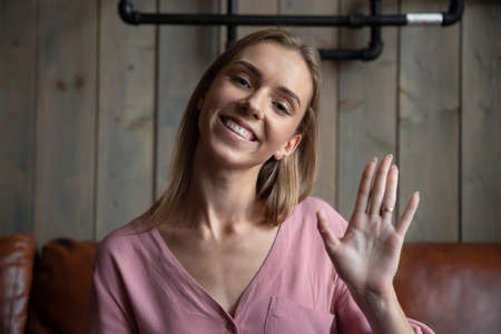 Headshot close up portrait of smiling Caucasian millennial woman wave at camera greeting talking on...