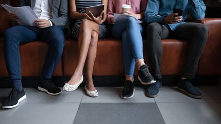 Close up of diverse multiethnic young people sit on couch waiting for job interview in office,...