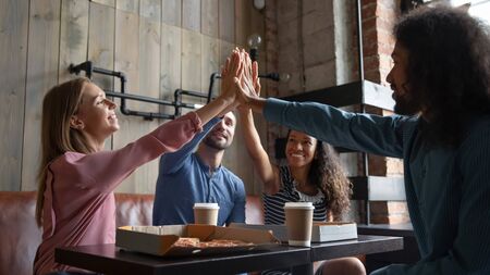 Overjoyed multiracial young people gather in cafe give high five showing unity and friendship, happy...