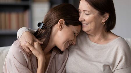 Smiling mature mother hugging adult daughter close up, expressing love and care, family enjoying...
