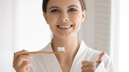 Portrait of smiling young Caucasian woman posing with toothbrush toothpaste recommend dental care, happy millennial girl show thumb up give recommendation or oral hygiene for healthy white teethの写真素材