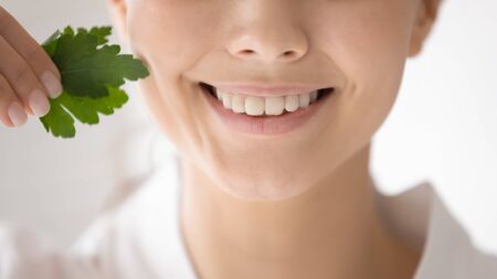 Crop close up of smiling young woman holding parsley recommend garnish for healthy white teeth, happy female freshen whiten tooth with natural green product for fresh breath, oral dental care conceptの写真素材