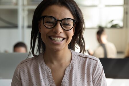 Close up headshot portrait picture of happy african american businesswoman with glasses. Smiling confident young diverse woman manager looking at camera on workplace background in office.の写真素材