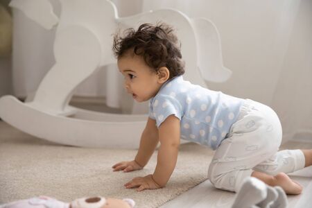 Cute little african American baby infant go on hands and knees on cozy warm wooden floor with...
