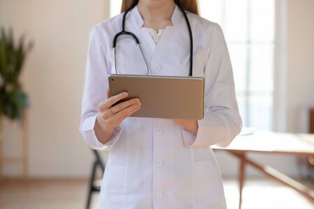 Close up of female physician in white medical uniform consult patient online using modern tablet, woman doctor or GP working on Pad, fill medical anamnesis on gadget, medicine and technology conceptの写真素材