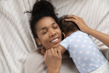 Close up top view of loving young african American mom lying in bed hug little infant baby, happy...
