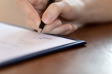 Close up of female patient put signature on paper document make health insurance agreement in...