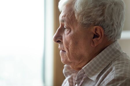 Profile close up view of sad lonely elderly man look in distance pondering or thinking, upset distressed senior grandfather feel loneliness and solitude, mourn or yearn at home or retirement houseの写真素材