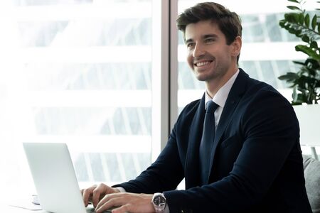 Confident business man sitting at desk in modern luxury office in front of laptop looking at...