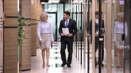 Male employee subordinate and businesslady boss chatting walk in office hallway. Full length mature...
