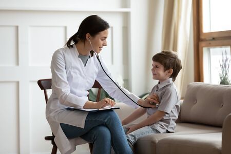 Young female pediatrician or GP listen to small boy patient heart with stethoscope at consultation...