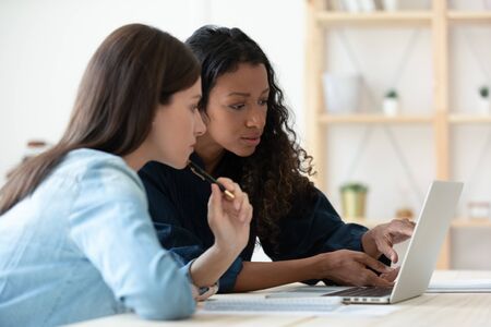 Confident young african american businesswoman talking with female mentor in coworking boardroom at meeting. Serious mixed race woman managers looking new business concept using laptop.の写真素材
