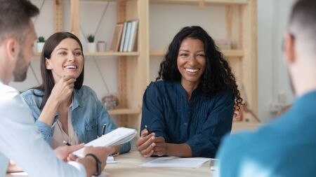 Happy african american businesswoman telling employees about project sit at table in coworking...