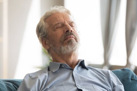 Head shot close up peaceful serene hoary middle aged mature man relaxing on comfortable couch with closed eyes. Happy senior old retired grandfather sleeping, enjoying stress free time on sofa.の写真素材
