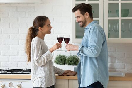 Happy millennial couple tenants clink glasses cheers feel excited moving into new home together, smiling young husband and wife celebrate relocation to own house, enjoy romantic date in kitchenの写真素材