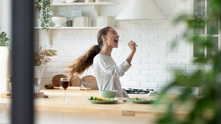 Funny millennial girl cooking at home have fun dancing singing in modern design kitchen, happy overjoyed young woman preparing food enjoy leisure domestic weekend in new apartment or houseの写真素材