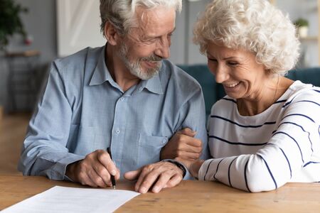 Happy senior older married couple discussing investing saving before signing paper agreement. Smiling middle aged man woman putting signature on marriage contract or making testate at lawyer office.の写真素材