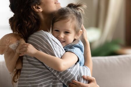 Close up loving mother hugging smiling adorable little daughter, expressing care and protection,...